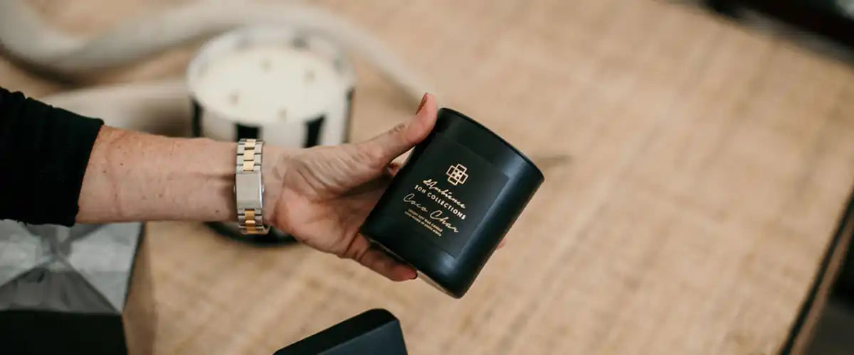 A black candle in a dark, cylindrical container with a decorative gold emblem.