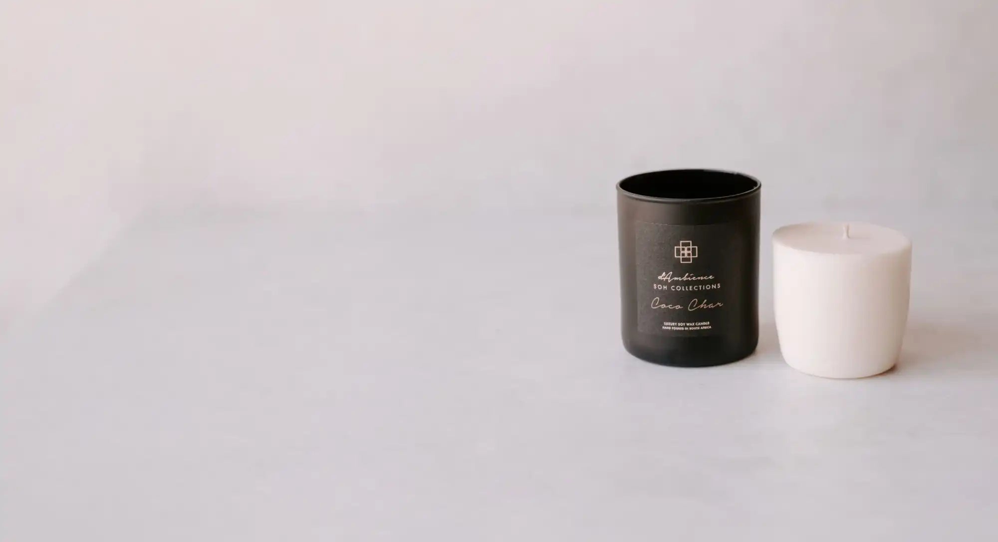A black candle in a jar next to a white pillar candle.
