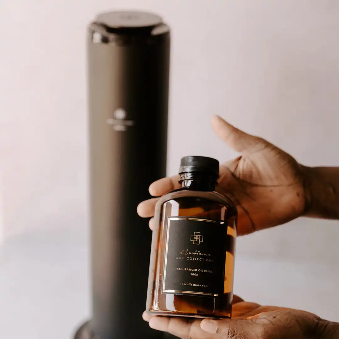 A person holding a dark amber bottle of fragrance oil with a black label.