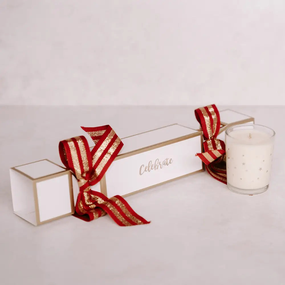 Festive Christmas cracker in white and gold with red ribbon and glass candle