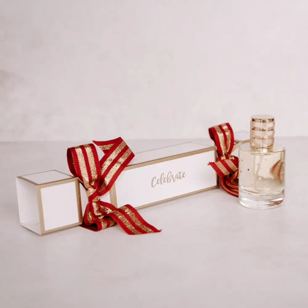 Festive white and gold Christmas cracker with red ribbon bow and glass perfume bottle
