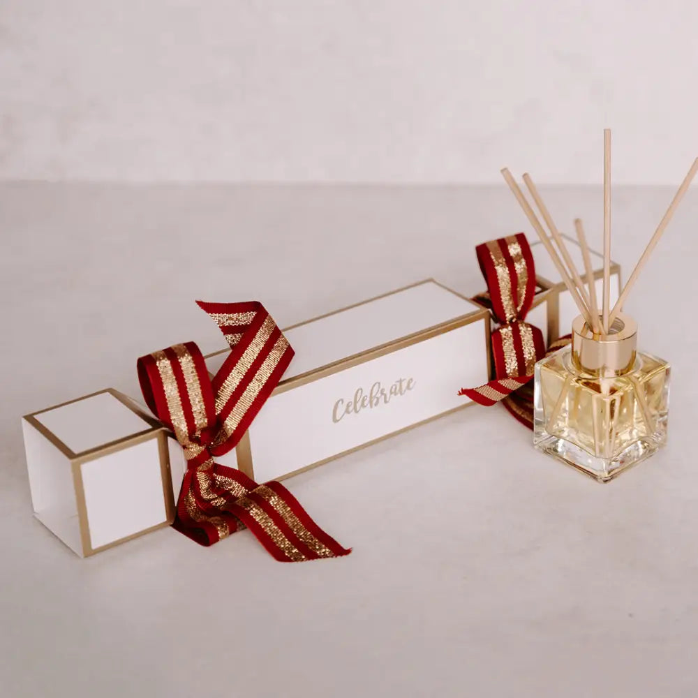 Festive Christmas cracker with gold trim, red and gold ribbon, and glass diffuser with reeds