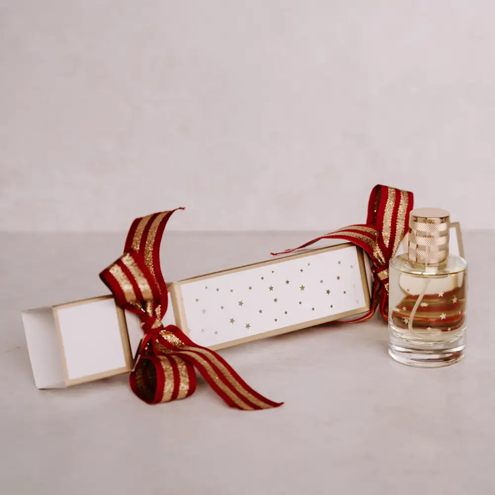 Festive Christmas cracker with gold stars and ribbon next to a glass perfume bottle