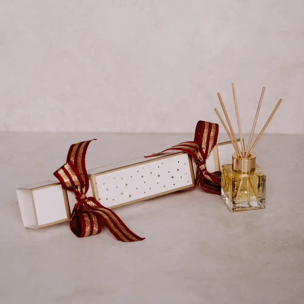 Festive white Christmas cracker with red and gold ribbon and gold reed diffuser