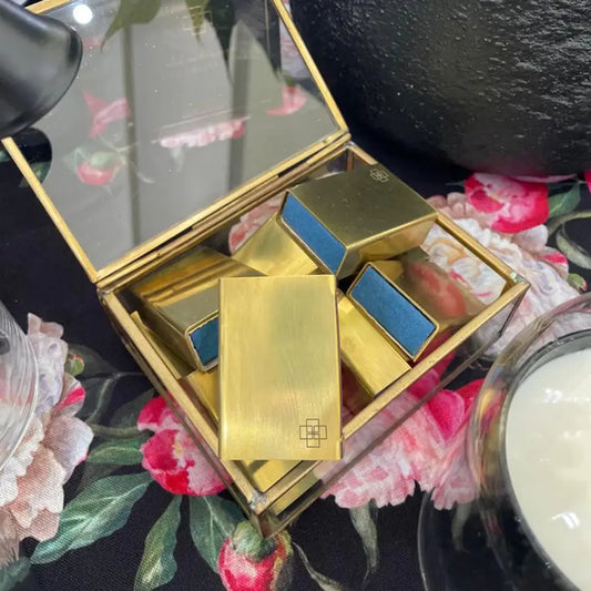 Brass-colored matchbox holder with clear lid filled with gold and blue scent diffuser containers