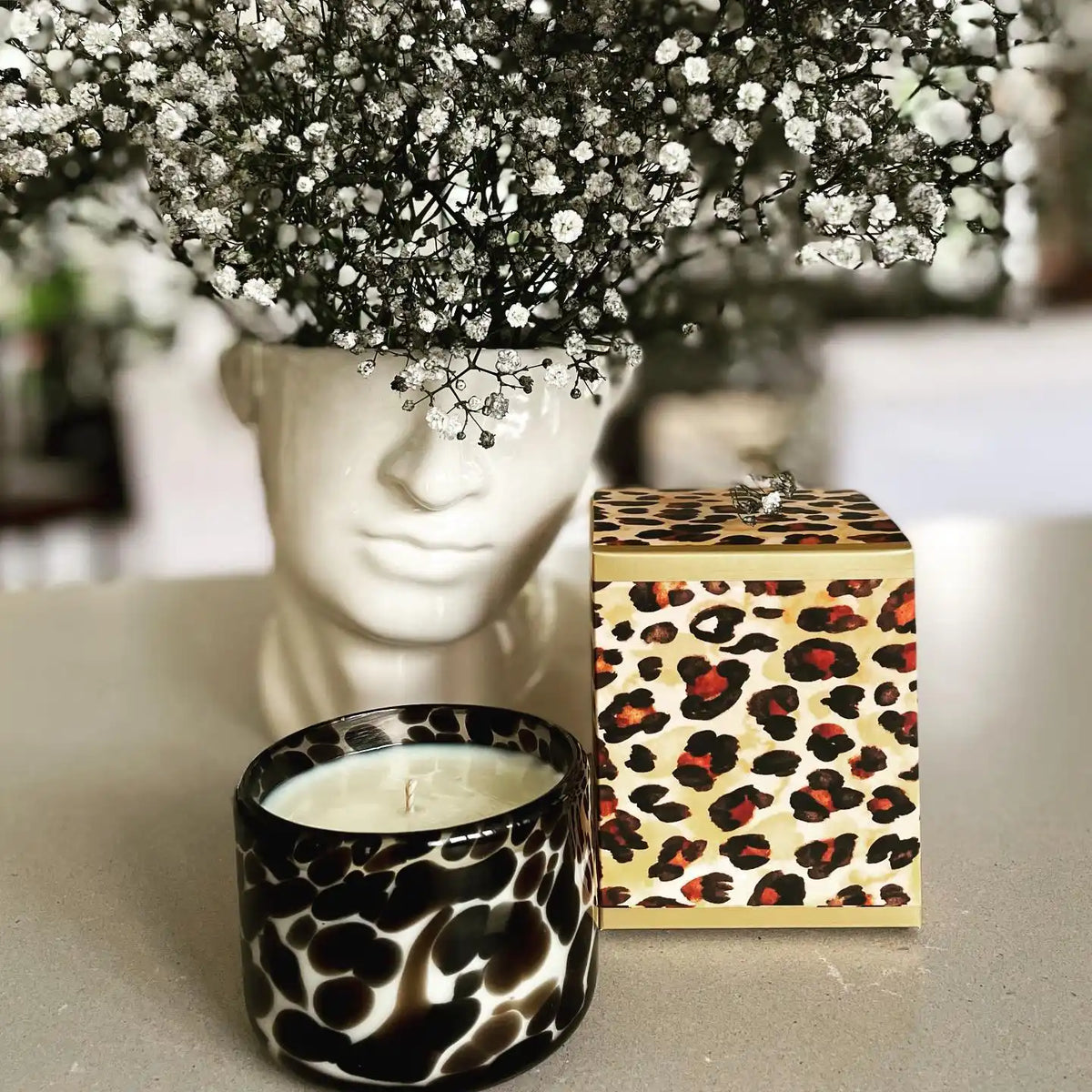 A white ceramic bust planter filled with baby’s breath flowers, a black and white spotted glass candle, and a leopard print box.